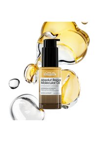 El aceite molecular Absolut Repair de L'Oréal en un envase transparente de color ámbar con un dosificador negro. Alrededor hay gotas de aceite de diferentes tamaños.