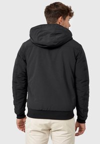 Black hooded jacket with a quilted design, ribbed cuffs, and hem. Seen from the back, featuring a smooth texture and minimal detailing.