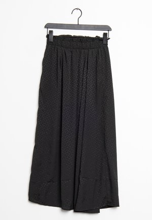 Jupe midi noire à pois subtils, avec ceinture élastique et tissu froncé, suspendue sur un cintre noir sur fond blanc.