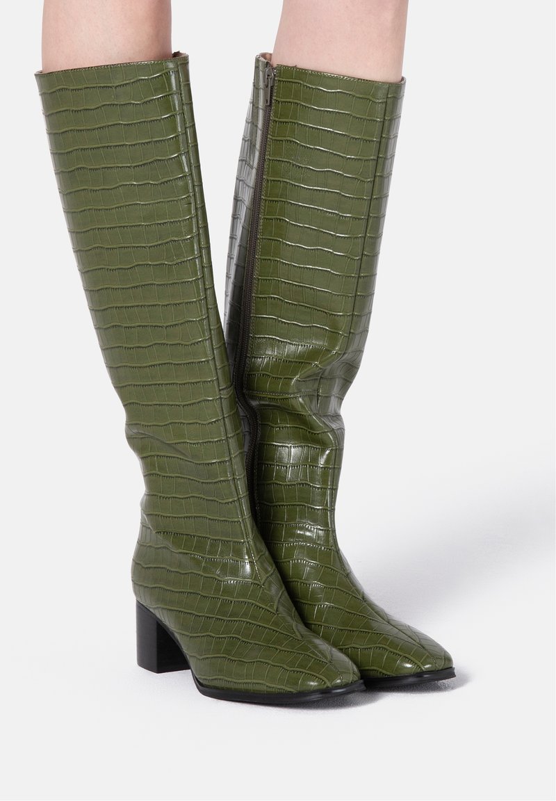 Bottes hauteur genou en simili cuir vert brillant avec texture crocodile, dotées d'un bout carré et d'un talon bloc. Détail zippé sur le côté.