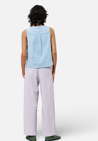 Helles blau-gestreiftes ärmelloses Oberteil, kombiniert mit helllila gestreiften, weit geschnittenen Hosen mit entspannter Passform und sichtbarer Stoffstruktur.