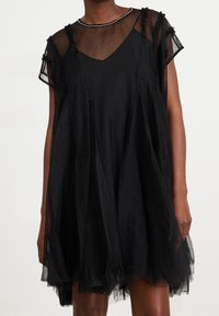Czarna sukienka z przezroczystym materiałem, dekoltem w kształcie V, postrzępionym wykończeniem, krótkimi rękawami oraz warstwową spódnicą z tiulu, zdobiona koralikowym detalem przy dekolcie.