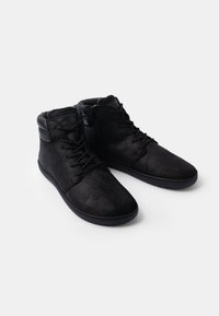 Mustad mustad ankle'ide jalatsid, mis on valmistatud pehmest sahari materjalist, millel on nööridega eesmine sulgemine, küljepealne tõmblukk ja sile kummitald.
