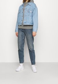 Ljusblå denimjacka, grå huvtröja, urtvättade blå jeans och vita sneakers. Funktioner inkluderar fickor och knappstängningar.