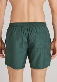Tmavě zelené plavkové šortky s elastickým pasem, bočními kapsami a zadní kapsou. Hladká nylonová tkanina s lehkou texturou.
