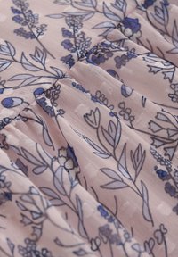 Hellrosa Stoff mit einem floralen Muster in verschiedenen Blautönen. Die Textur wirkt weich mit feinen Falten und zarten Details.