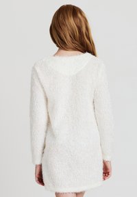 Abito maglione bianco e soffice con maniche lunghe, scollatura rotonda e finitura testurizzata. L'orlo termina sopra la metà della coscia.