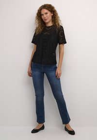 Black lace top with short sleeves featuring floral patterns, paired with blue fitted jeans and black ballet flats.