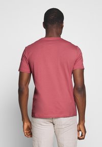 T-shirt z krótkim rękawem i okrągłym dekoltem w stonowanym różowym kolorze; miękki materiał bawełniany o gładkiej fakturze; dopasowany krój, minimalne detale szwów.