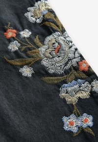 Broderie florale avec des fleurs blanches, bleues, orange et beiges ainsi que des feuilles vertes sur un tissu en denim foncé.