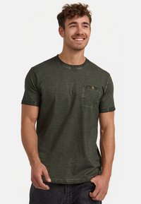 Grünes kurzärmeliges T-Shirt aus einem weichen, strukturierten Stoff. Verfügt über einen runden Ausschnitt und eine linke Brusttasche mit einem Knopfdetail.