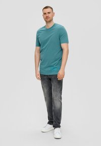 Teal korte mouwen t-shirt met een ronde halslijn, gecombineerd met vervaagde zwarte jeans en witte sneakers. Eenvoudig ontwerp zonder zichtbare patronen.