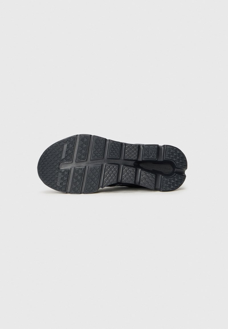 Suela de zapatilla negra con agarre texturizado, que presenta patrones geométricos, ranuras de flexión y una puntera redondeada para tracción y soporte.