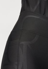 Close-up of black high-waisted leggings showing side pocket and subtle tonal patterns on the fabric.