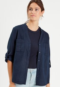 Chemise bleu marine à boutonnière avec un col, deux poches poitrine et des manches retroussées. Tissu léger, tissé avec une coupe décontractée.