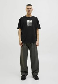 Black t-shirt with a graphic print in the center, short sleeves, relaxed fit, paired with dark green wide-leg trousers and black shoes.