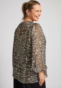 Blusa con stampa leopardata, maniche lunghe e gonfie, dettaglio a chiave sul retro e tessuto trasparente. Toni terra di beige, marrone e nero.