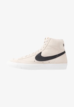 Baskets montantes en daim beige avec semelle blanche et virgule noire Nike sur le côté, lacées, montrées de profil droit.