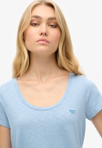 Lichtblauw T-shirt met korte mouwen van zacht materiaal. Heeft een ronde halslijn en een klein geborduurd logo op de borst. Soepele textuur.