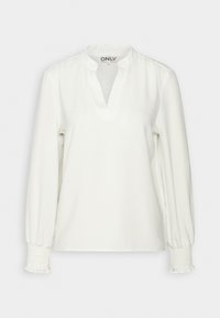 Blouse blanche à manches longues avec col bande, ouverture en V et poignets smockés, présentée sur un fond uni.