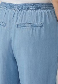 Pantalons bleu clair à taille élastique avec une texture lisse, dotés de deux poches arrière et d'une ceinture froncée pour plus de flexibilité et de confort.