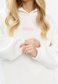 Felpa bianca con logo ricamato rosa. Caratterizzata da un tessuto morbido, polsini oversize e cappuccio con cordino. Eccelle per il suo design minimalista.