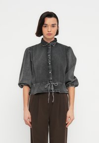 Μαύρο πουκάμισο από τζιν με φουσκωτά μανίκια, κουμπιά στο μπροστινό μέρος, γιακά, ρυθμιζόμενο κορδόνι στη μέση και αντιθετικές λεπτομέρειες ραφής.