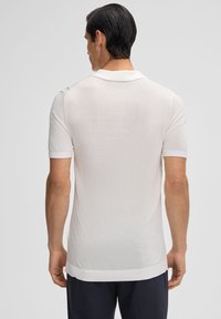 Polo shirt bianco a maniche corte con colletto e polsini a coste. Texture morbida, orlo dritto e motivo a maglia sottile. Vista posteriore mostrata.