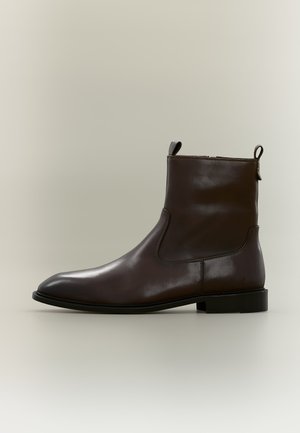 Bottine en cuir marron foncé avec fermeture éclair latérale, languettes en haut, petit talon et bout arrondi, présentée sur un fond neutre.
