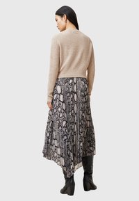 Maglione lavorato a maglia beige con orlo a coste aderente, indossato sopra un abito lungo a stampa serpente bianco e nero, abbinato a stivali neri fino al ginocchio.