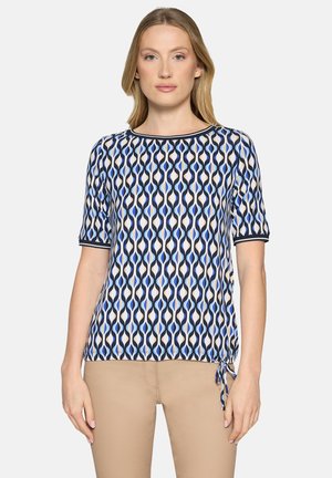 Kortemouws top van lichte stof met een golfpatroon in blauw, marineblauw en crèmekleur. Heeft een ronde halslijn en een verstelbaar koorddetail bij de zoom.