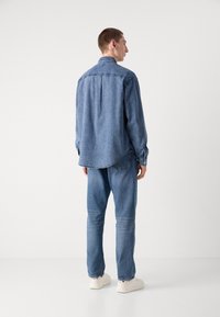 Lichtblauwe denim shirt met een rechte snit, lange mouwen en een rugplooi-detail, gecombineerd met bijpassende lichtblauwe jeans en witte sneakers.
