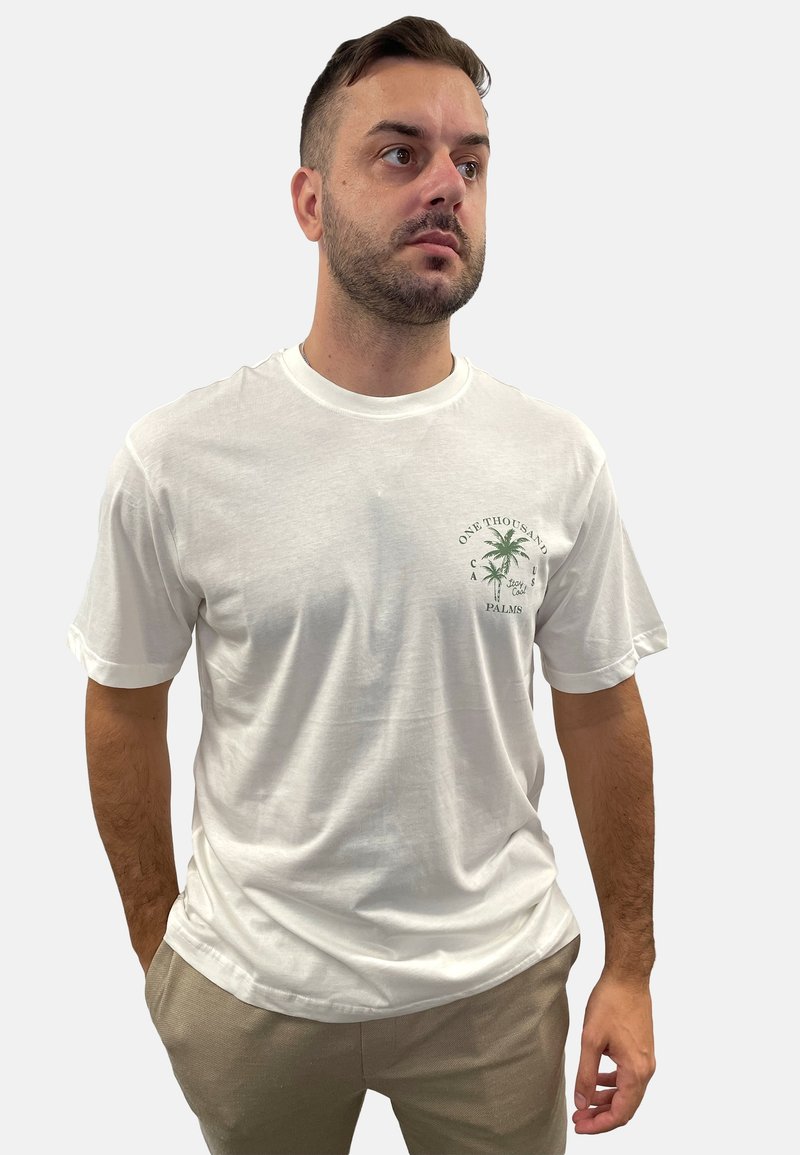 Weißes Baumwoll-T-Shirt mit kurzen, umgeschlagenen Ärmeln, das ein grünes Palmbaum-Motiv auf der linken Brust und einen lockeren Schnitt hat.