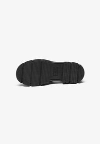Black rubber shoe sole with a textured surface featuring horizontal grooves and circular accents, designed for traction and durability.