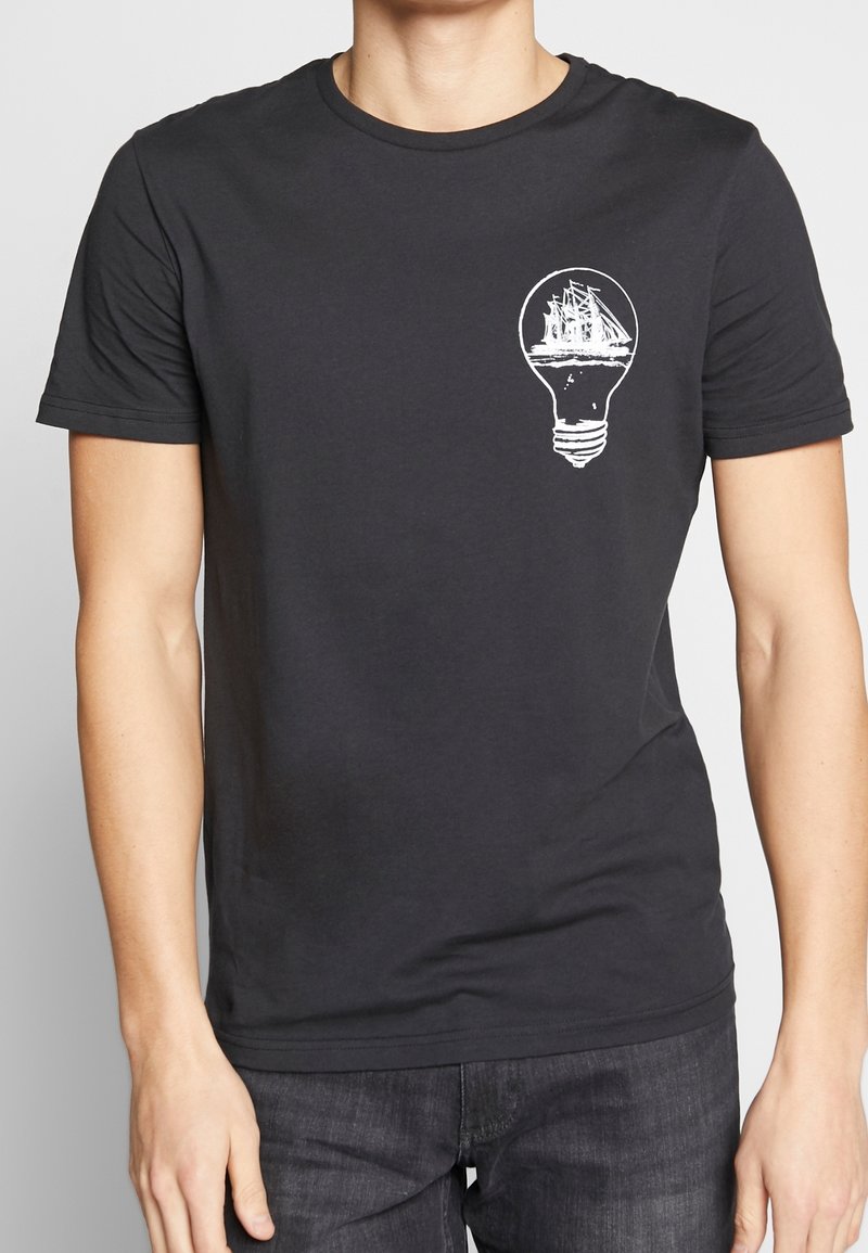 T-shirt en coton noir avec un graphique blanc représentant un bateau à l'intérieur d'une ampoule. Manches courtes et design à col rond.