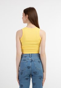 Žlutý žebrovaný crop top v kombinaci s modrými džíny s vysokým pasem, které mají vzor srdcí. Oblečení má přiléhavý design s hladkou texturou.