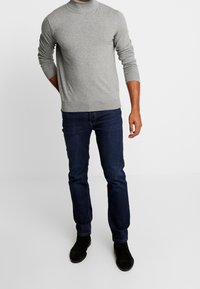 Grauer, langärmeliger Rollkragenpullover aus weichem Stoff, kombiniert mit dunkelblauen Jeans und schwarzen Stiefeletten.