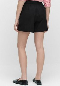 Svarta shorts i lättviktsmaterial, med resårmidja, rak skärning och en slät textur. Bärs med svarta ballerinas.