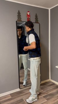 Μαύρο και μπλε γιλέκο με σχέδια πάνω σε λευκό πουκάμισο, συνδυασμένο με ανοιχτό μπλε σκισμένα τζιν και γκρι αθλητικά παπούτσια. Ολοσωμος καθρέφτης εμφανίζεται.