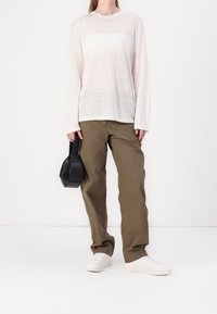 Chemise blanche à manches longues avec des rayures transparentes, pantalon vert olive, baskets blanches, et un petit sac à main noir avec une poignée.
