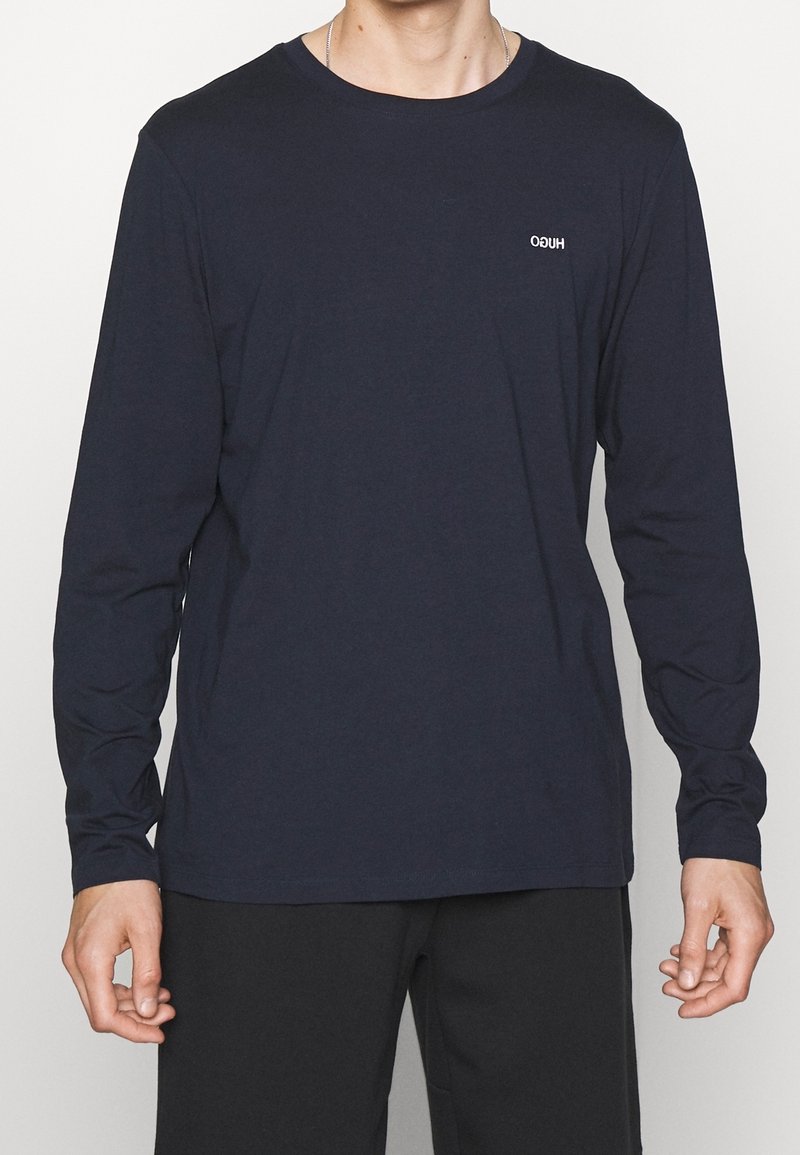 Navyblaues T-Shirt mit langen Ärmeln aus weichem Stoff, ausgestattet mit einem runden Ausschnitt und einem kleinen weißen Logo auf der linken Brustseite.