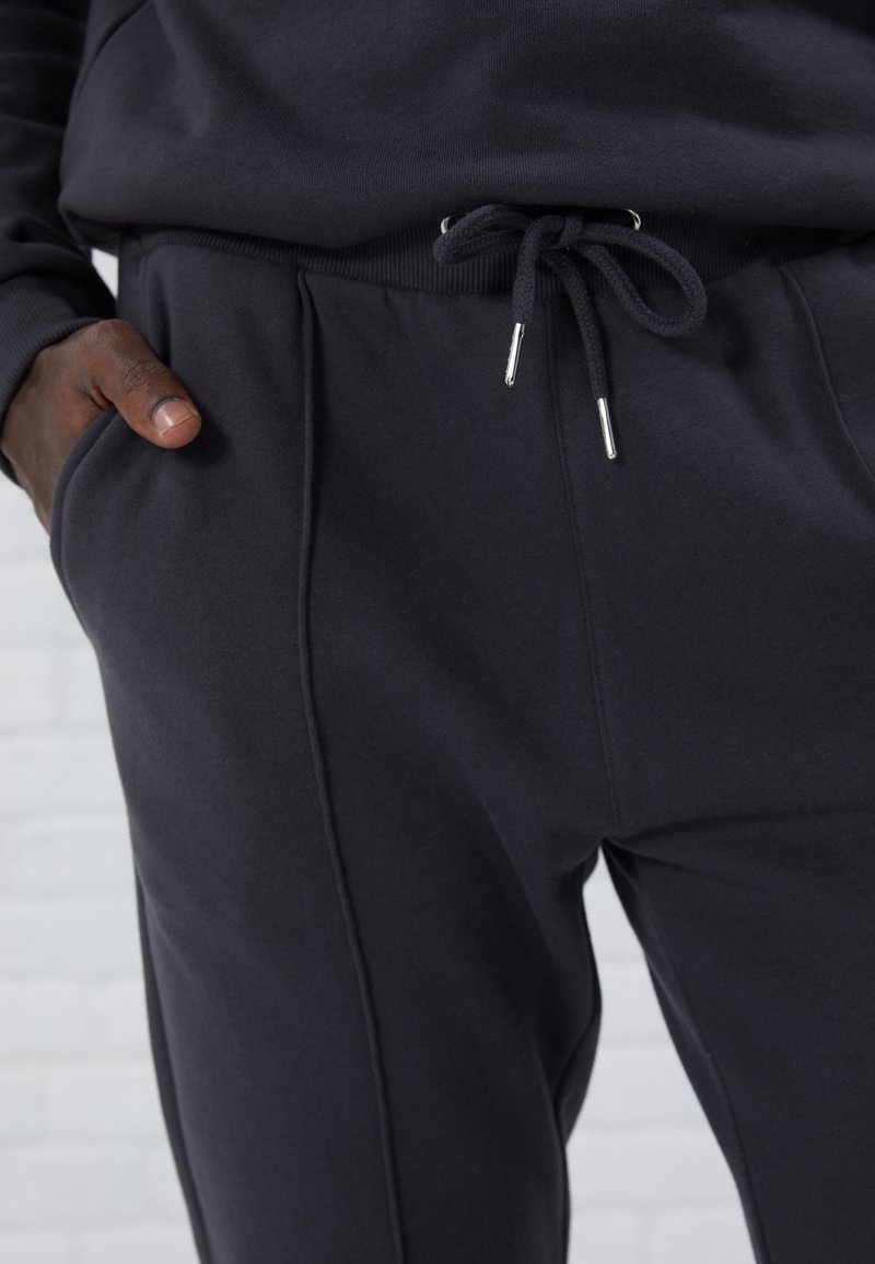 Pantalons de survêtement noirs en tissu doux, dotés d'une taille élastique avec cordon de serrage, de poches latérales et d'une texture lisse.
