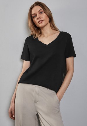 T-shirt noir à manches courtes en V en tissu doux, avec une coupe décontractée. Associé à un pantalon de couleur claire, design minimaliste sans motifs.