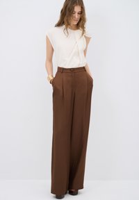 Beige top met geplooide details en korte mouwen, gecombineerd met hoogwaist, wijde bruine broek met zijzakken en een knoopsluiting.
