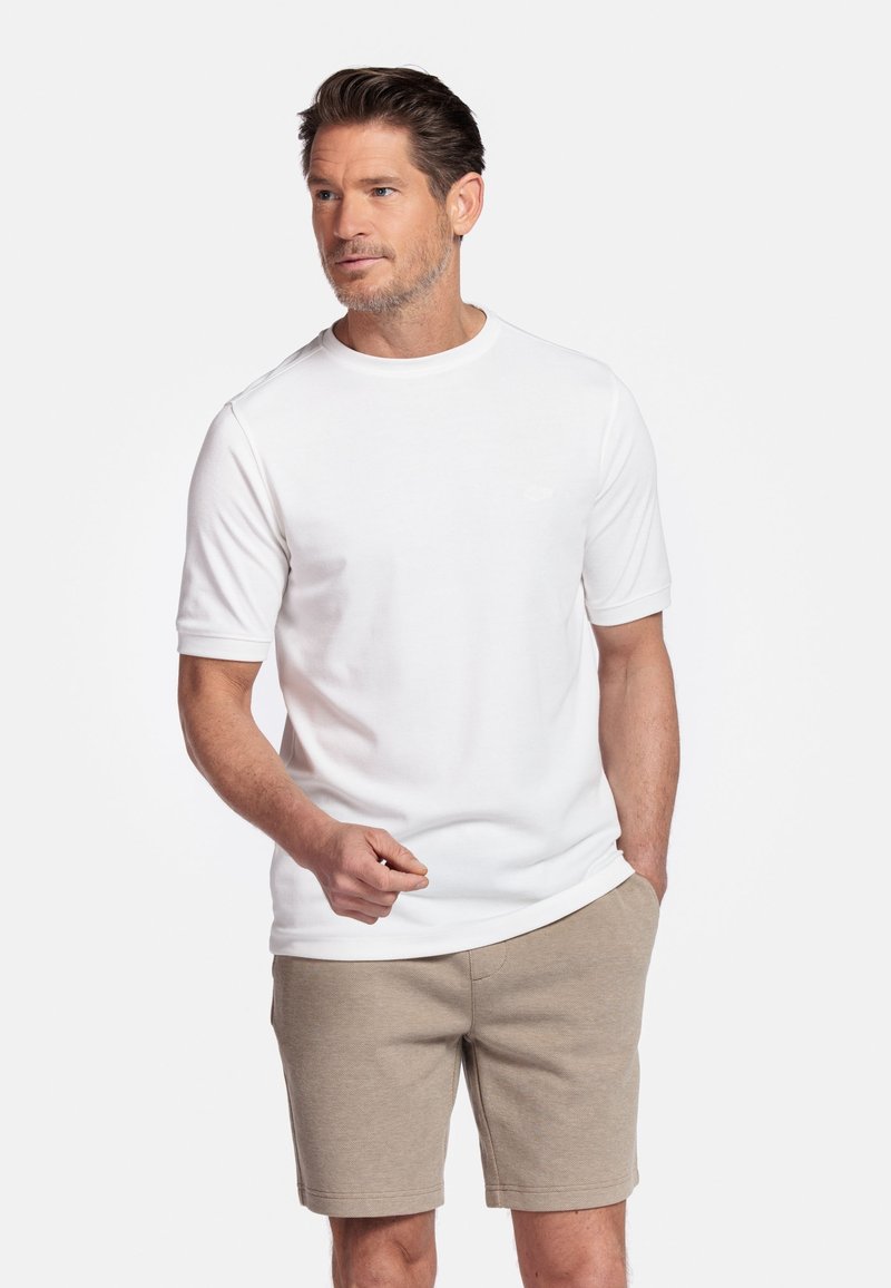 Weißes T-Shirt mit kurzen Ärmeln und rundem Ausschnitt, aus glattem Baumwollstoff, kombiniert mit beigen Shorts, vor einem schlichten Hintergrund stehend.