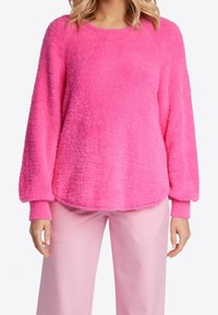 Pullover rosa fuzzy con scollo a girocollo e maniche lunghe. Presenta polsini a coste e una vestibilità rilassata, abbinato a pantaloni a strisce rosa chiaro.