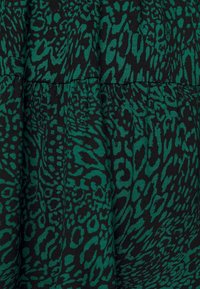 Svart tyg med ett grönt abstrakt djurmönster. Texturen verkar slät, med sammangruppade sektioner som skapar en flödande design.