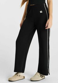 Zwarte wijde broek met witte zijstroken en een reliëflogo. Elastische tailleband, gladde stof en een relaxed fit.
