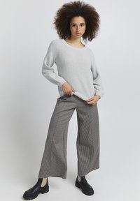 Hellgrauer Strickpullover mit langen Ärmeln und Rundhalsausschnitt, kombiniert mit weit geschnittenen, braun-karierten Hosen und schwarzen Plateaustiefeletten.