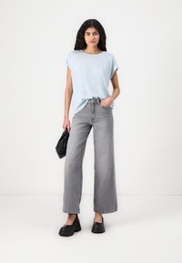 Lys blå og hvitstripete oversized t-skjorte med korte ermer, kombinert med høytlivede grå vide jeans. Svart håndbag, chunky svarte sko.